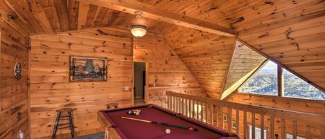 A wooden interior with a pool table, a ladder, and a railing.