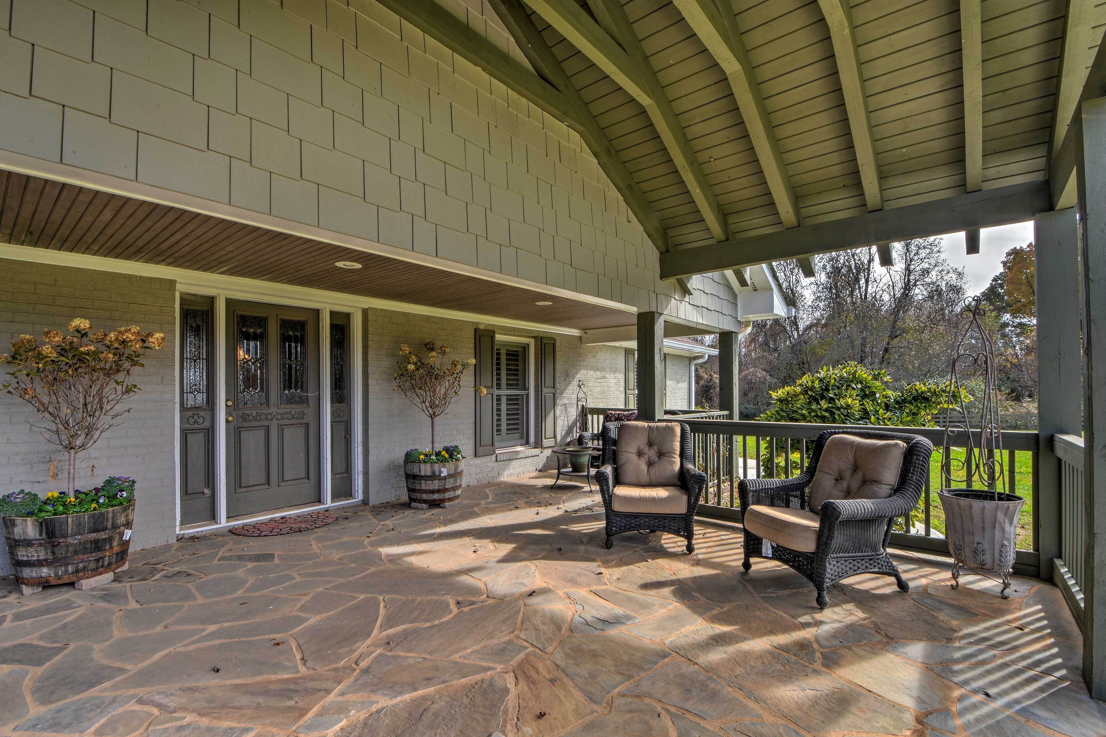 A covered patio area with stone flooring, wicker furniture, and potted plants.