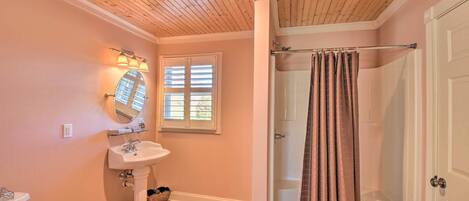 A bathroom with a wooden ceiling, a pedestal sink, a mirror, a window with blinds, and a shower curtain.