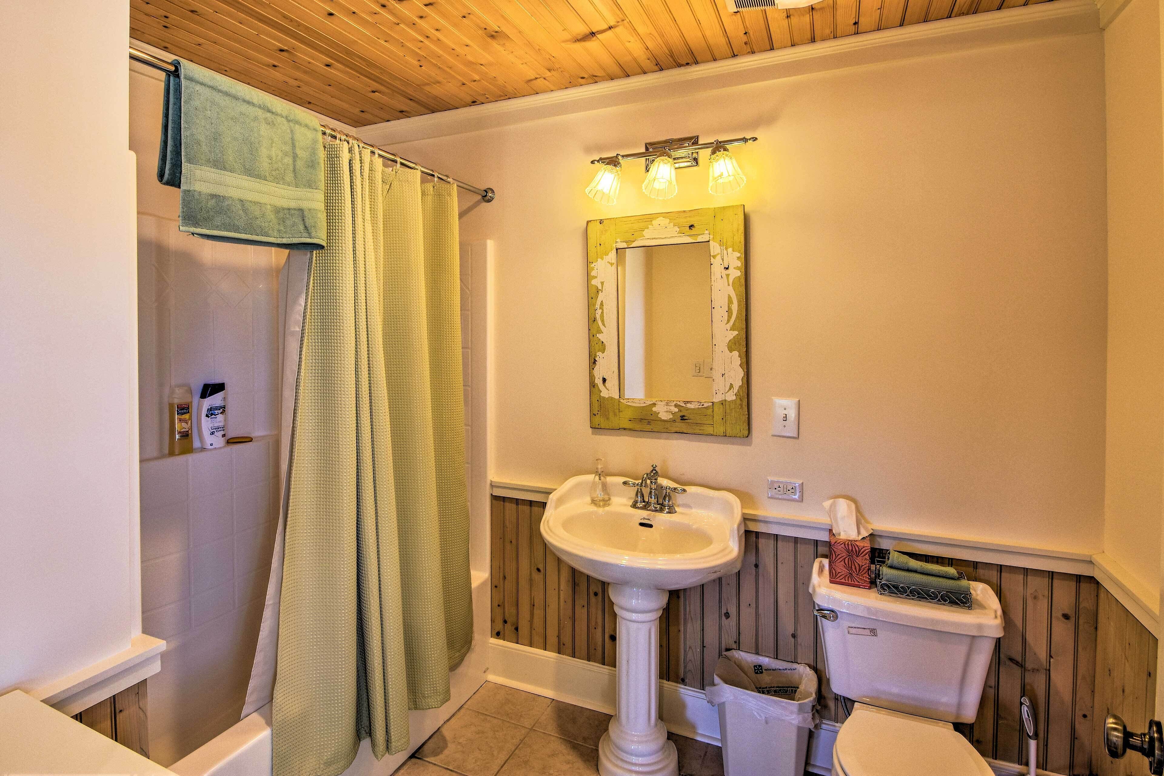 A bathroom with a pedestal sink, a toilet, and a shower with a green shower curtain.