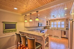 A kitchen with wooden ceiling, white cabinets, granite countertops, and bar stools.