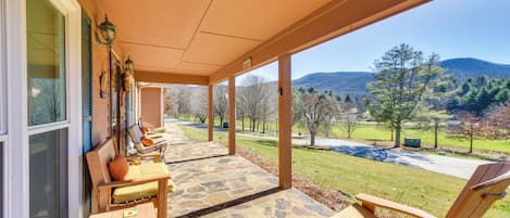 Un patio cubierto con piso de piedra, mobiliario de madera y vistas a un paisaje montañoso.