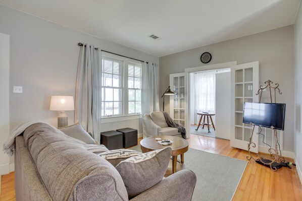 Una sala de estar con sofá, sillón, mesa de centro, lámpara, televisor y estantería.