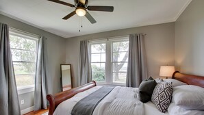 A bedroom with a large bed, a ceiling fan, and two windows with curtains. - Charming Cottage w/ Mississippi River Views! (Natchez)