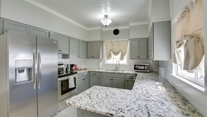 A modern kitchen with stainless steel appliances, a marble countertop, and light gray cabinetry. - Charming Cottage w/ Mississippi River Views! (Natchez)