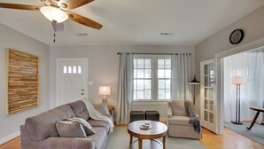 A living room with a ceiling fan, a wooden coffee table, a sofa, a chair, a lamp, and a window with curtains. - Charming Cottage w/ Mississippi River Views! (Natchez)