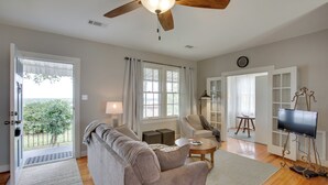 A spacious living room with a ceiling fan, a sofa, a coffee table, and a television on a stand. - Charming Cottage w/ Mississippi River Views! (Natchez)