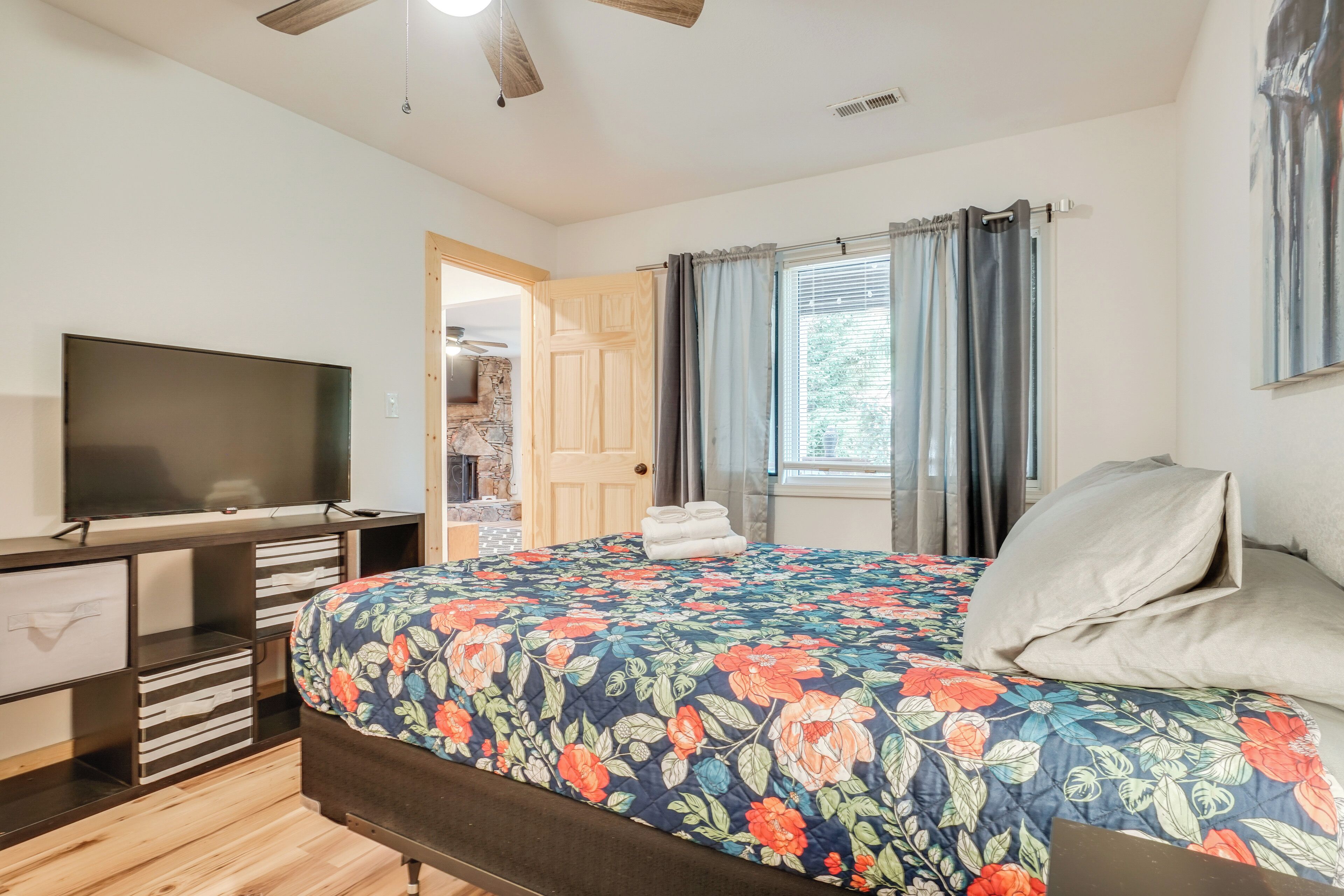 A bedroom with a bed, a TV, a wooden desk, and a stone fireplace.