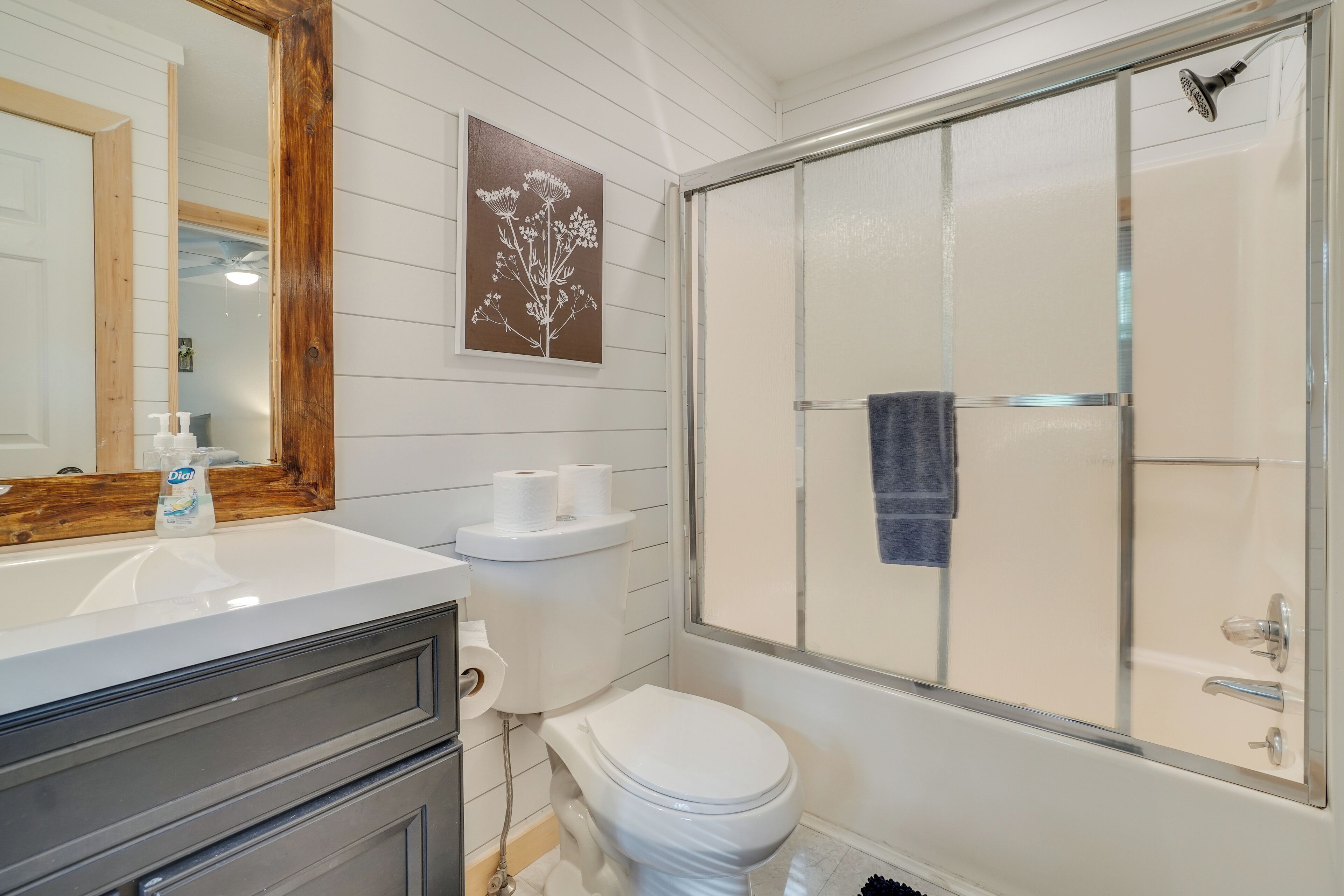 A bathroom with a white toilet, a sink with a mirror, a shower enclosure, and a framed picture on the wall.