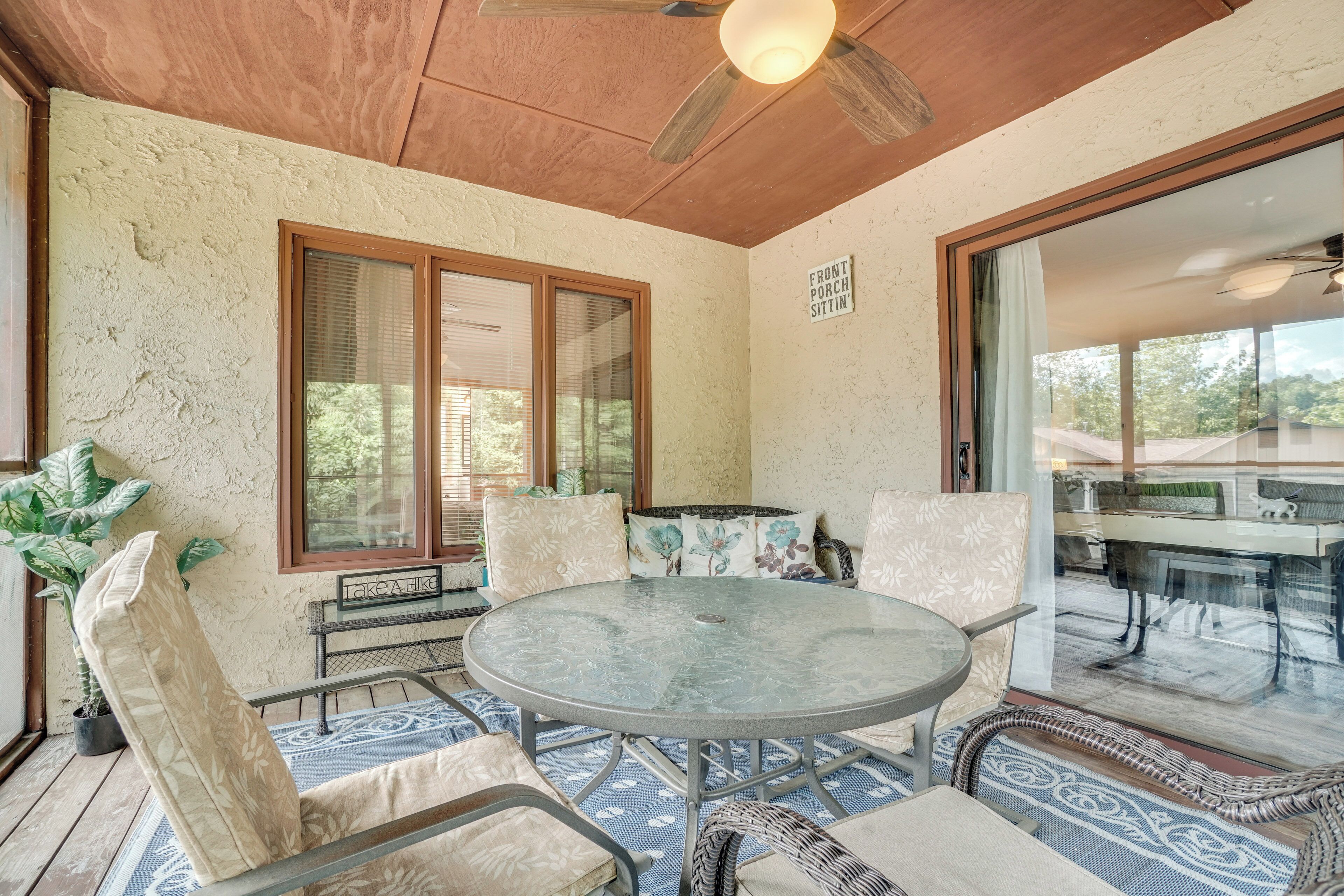 Une terrasse couverte avec une table ronde et des chaises, de grandes fenêtres et un ventilateur de plafond.