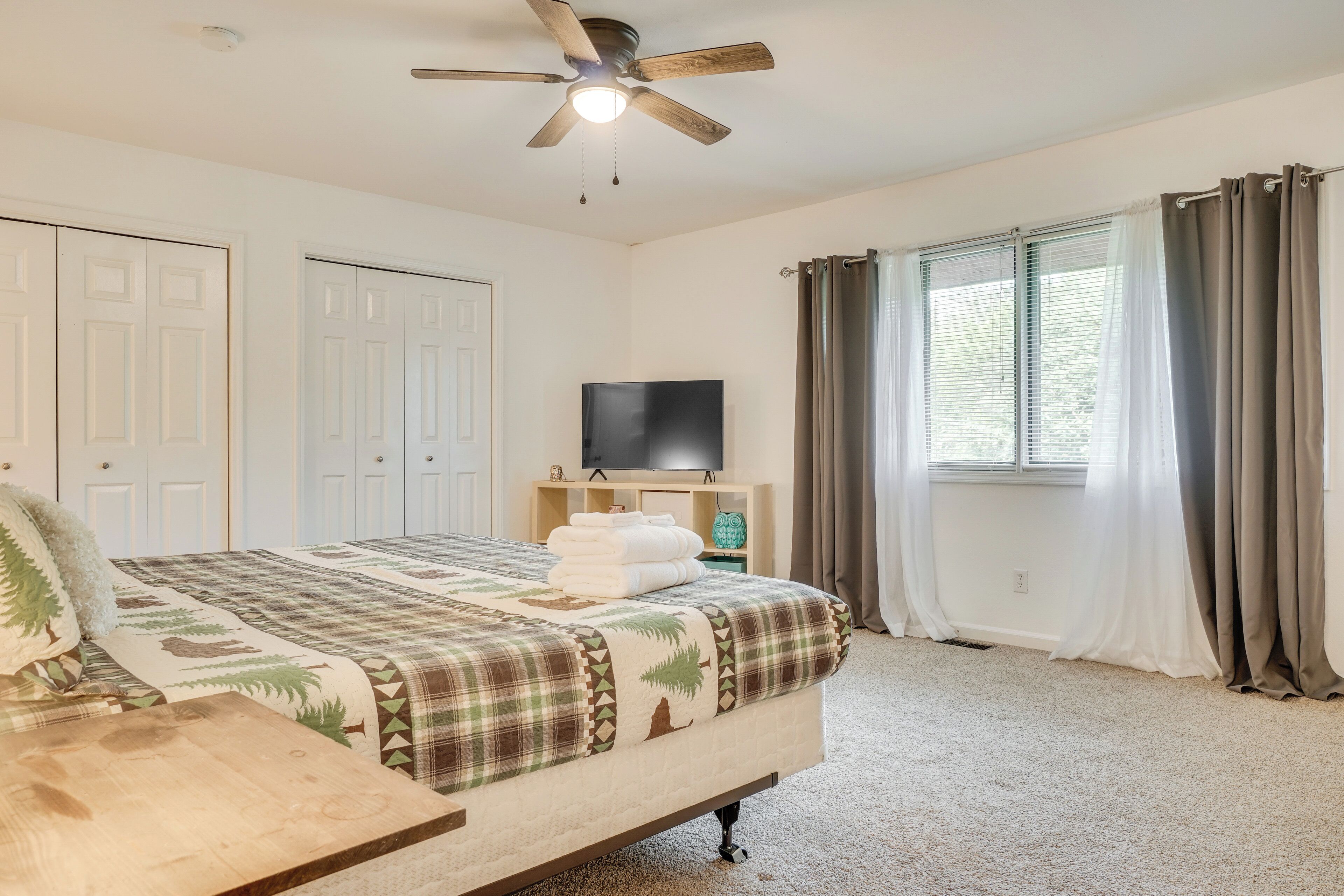 A bedroom with a bed, a ceiling fan, a TV, and a window with curtains.