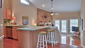 A kitchen with a central island, bar stools, a ceiling fan, and a stone accent wall.