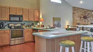 A kitchen with wooden cabinets, a microwave, an oven, a large island with stools, and a stone wall with a compass decoration.