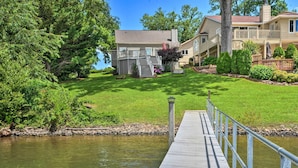 A waterfront property with a dock leading to a house with a deck and a covered patio.