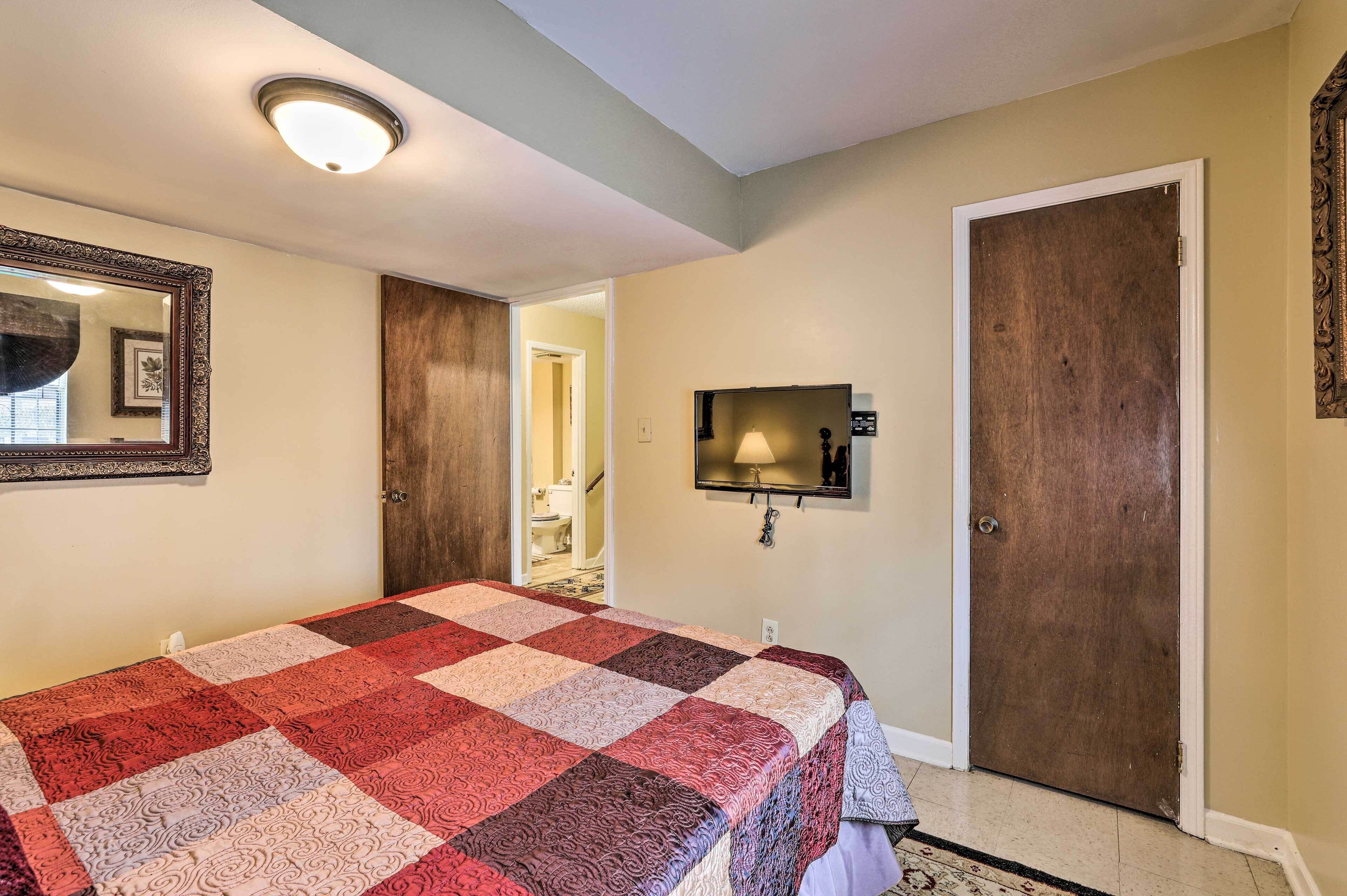 A bedroom with a large bed, a television mounted on the wall, and a door leading to a bathroom.