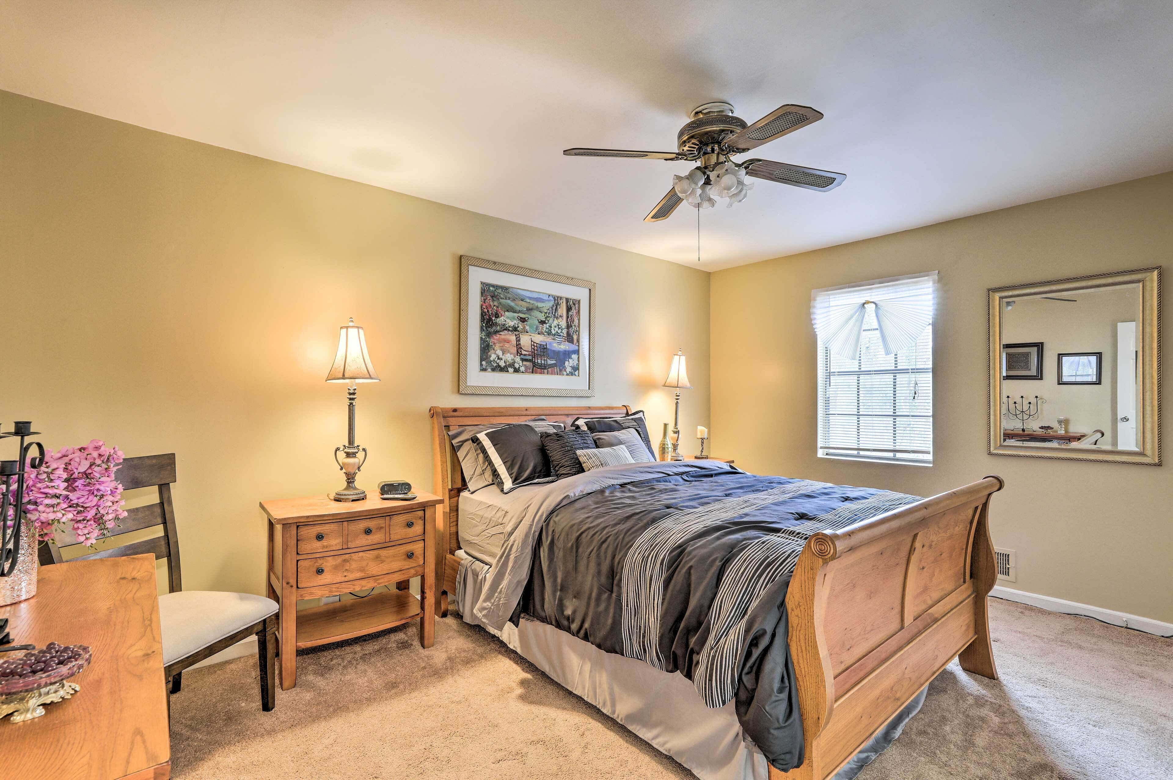 A bedroom with a bed, bedside tables, a ceiling fan, a window with blinds, and a framed picture on the wall.