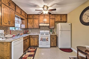 Une cuisine avec des meubles de rangement en bois, un réfrigérateur blanc, une cuisinière et un ventilateur de plafond.