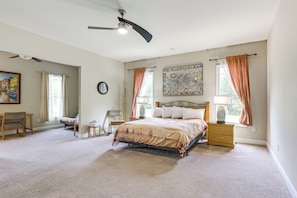 A bedroom with a bed, a desk, a chair, a window with curtains, a ceiling fan, and a wall clock.