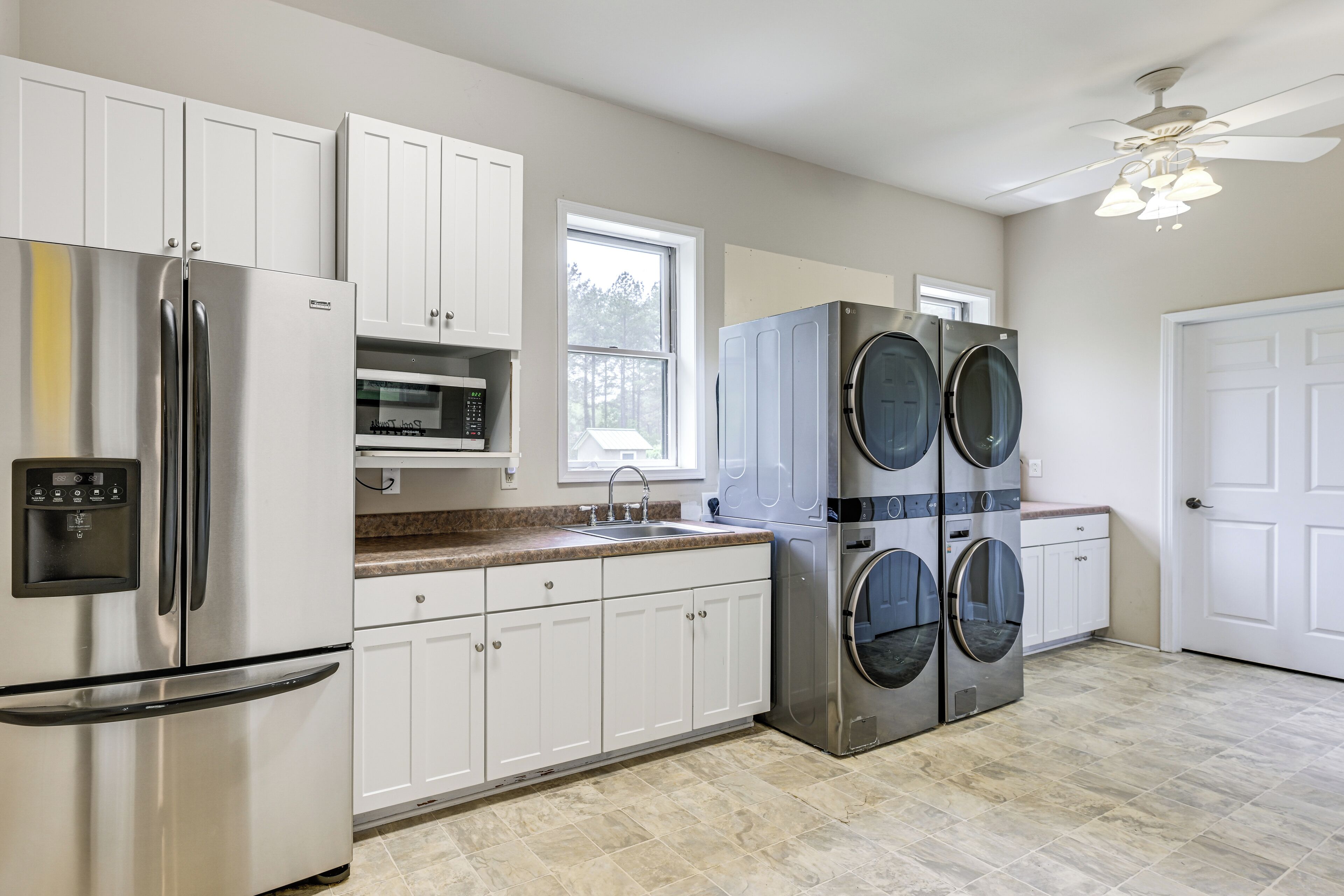 A kitchen with stainless steel appliances, white cabinets, a window, and a ceiling fan.