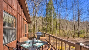 Un espace extérieur aménagé pour prendre les repas, avec une table pour deux, un barbecue et une vue sur la forêt environnante.
