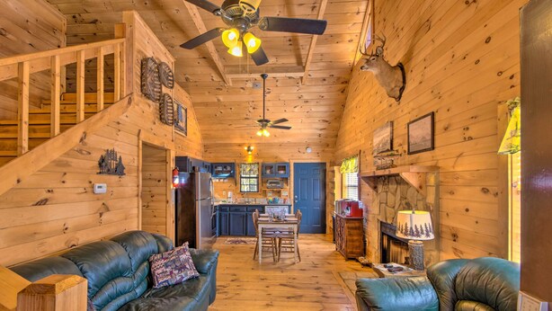 L’intérieur d’une cabane en rondins, avec un escalier, des canapés en cuir, un coin repas et une cheminée.