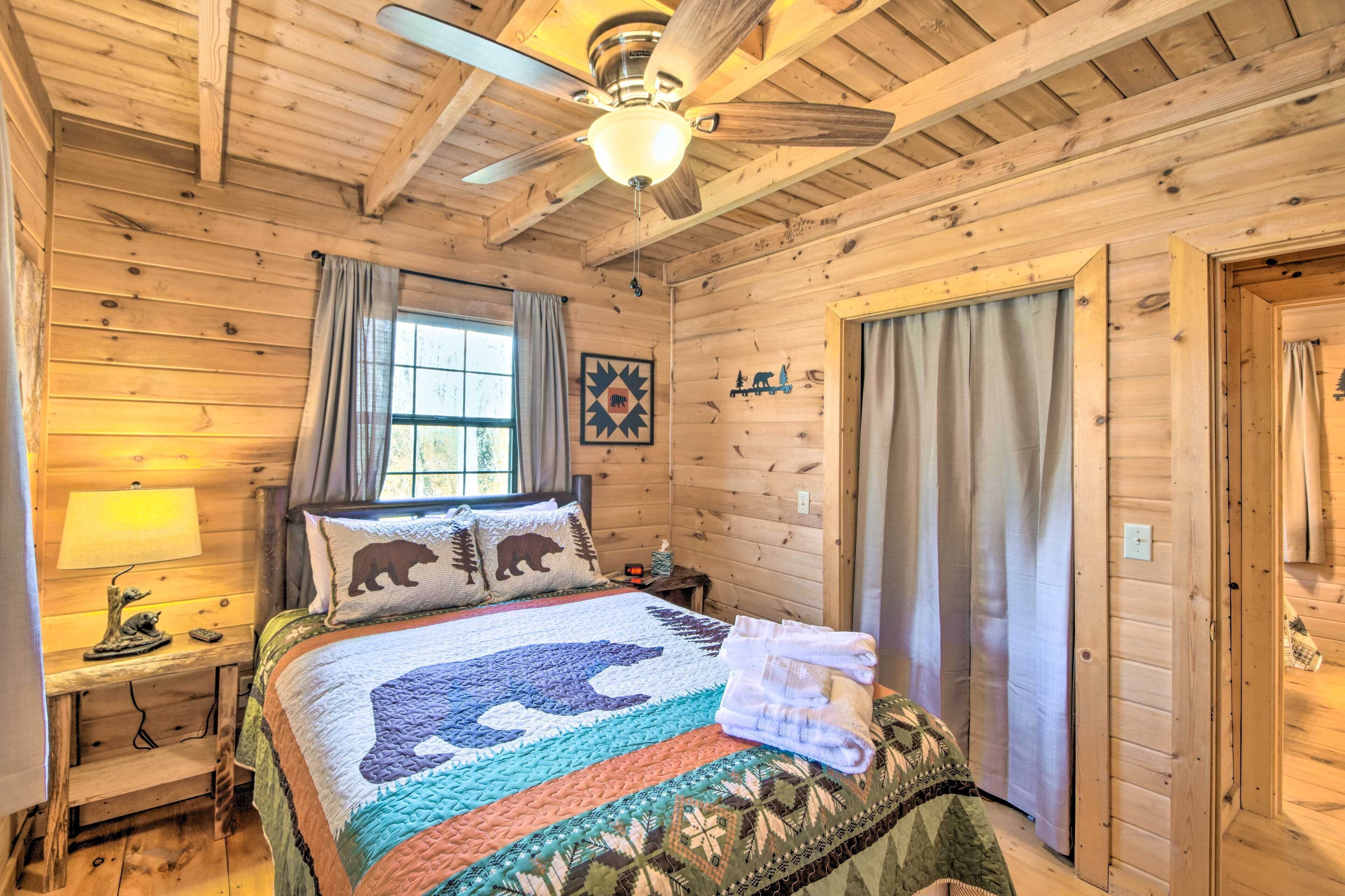 Ein gemütliches Schlafzimmer einer Holzhütte mit Bett, Deckenventilator, Fenster mit Vorhängen und Tür.