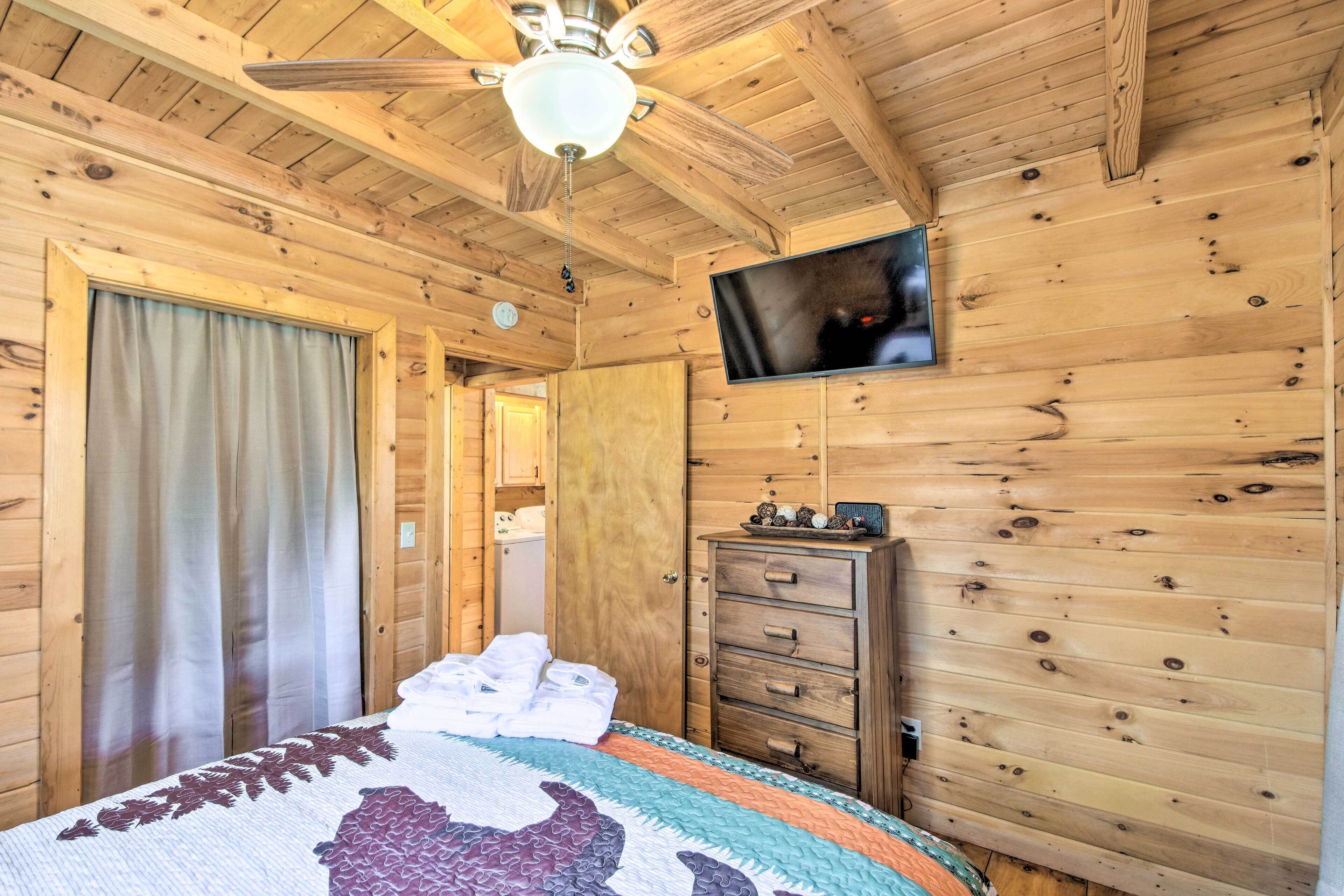 A wooden cabin bedroom with a bed, a dresser, a television, and a ceiling fan.