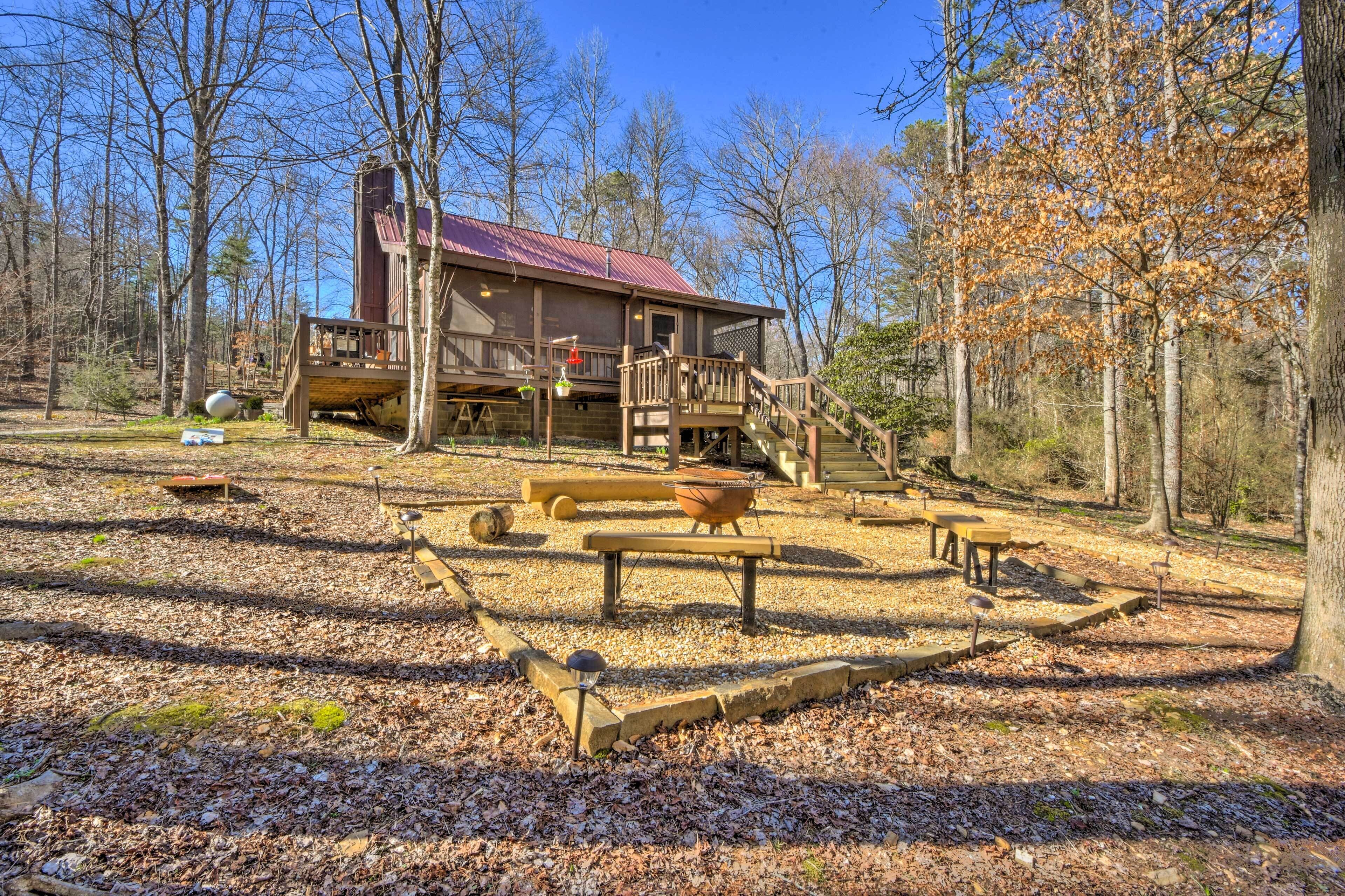 A rustic cabin with a wooden deck, a fireplace, and a large window overlooking a forested area.