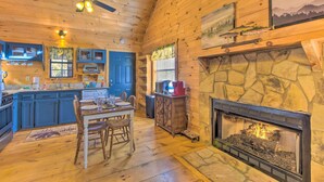 L’intérieur chaleureux d’un chalet avec une cheminée en pierre, un plafond en bois et un coin repas comprenant une table et des chaises.