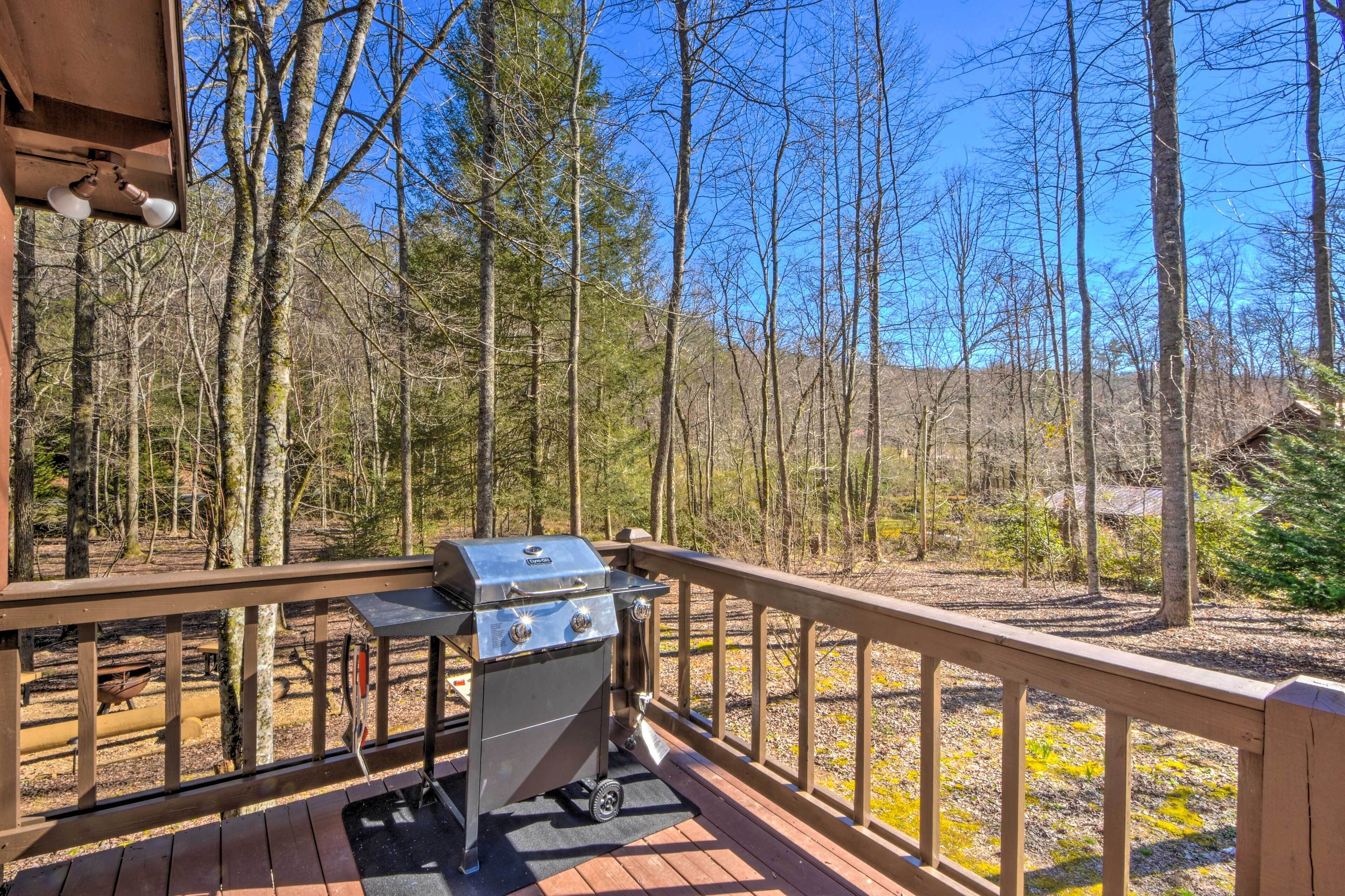 A deck with a barbecue grill, wooden railings, and a forested backdrop.