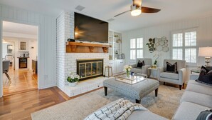 A spacious living room with a fireplace, a ceiling fan, and a large TV mounted on the wall. - Luxury Retreat in Smyrna: Pool, Pickleball & More! (Smyrna)