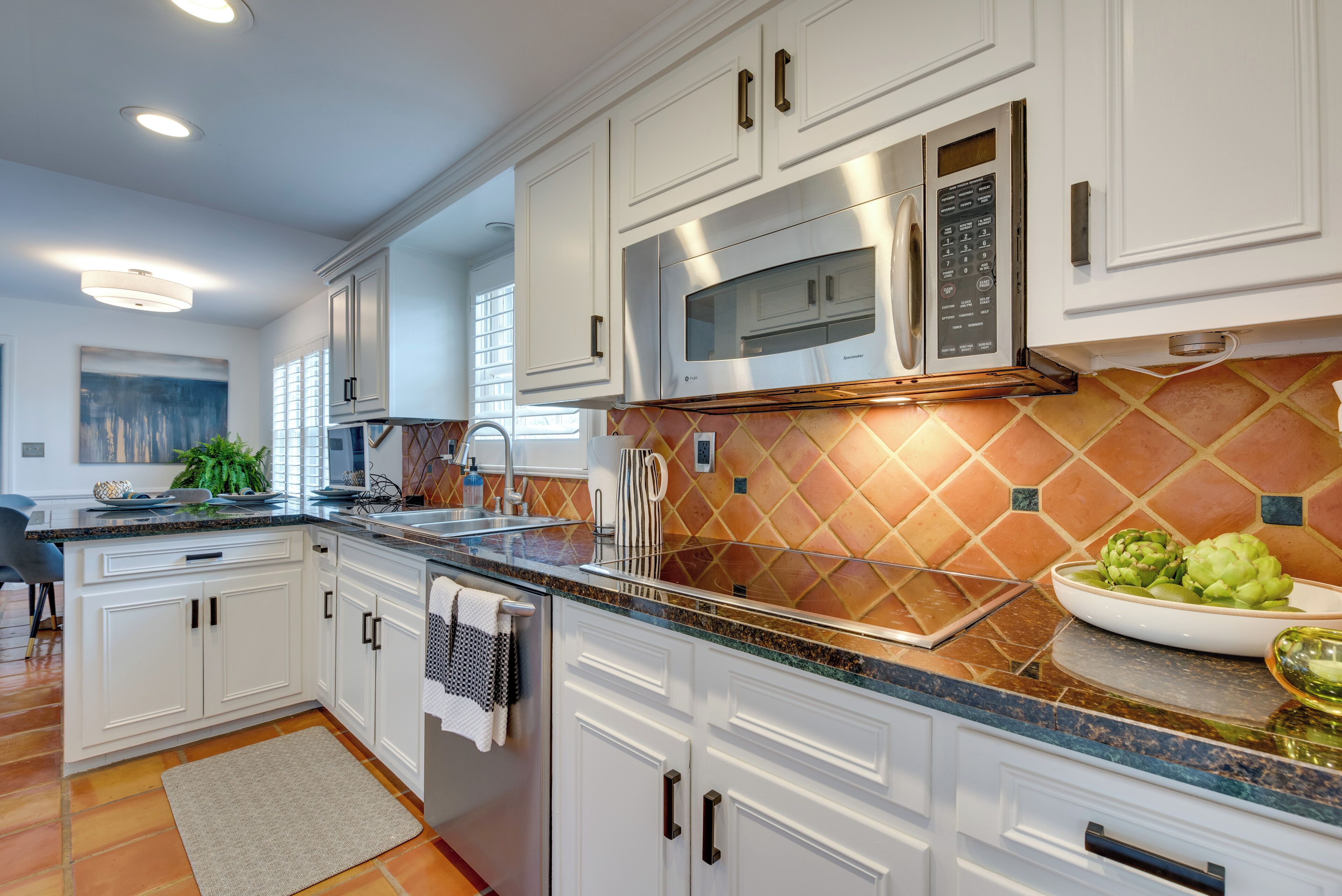 A modern kitchen with white cabinets, stainless steel appliances, and a patterned backsplash.