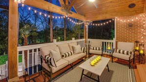 An outdoor patio with a wooden ceiling, string lights, a sofa, chairs, a table, and a lantern. - Luxury Retreat in Smyrna: Pool, Pickleball & More! (Smyrna)