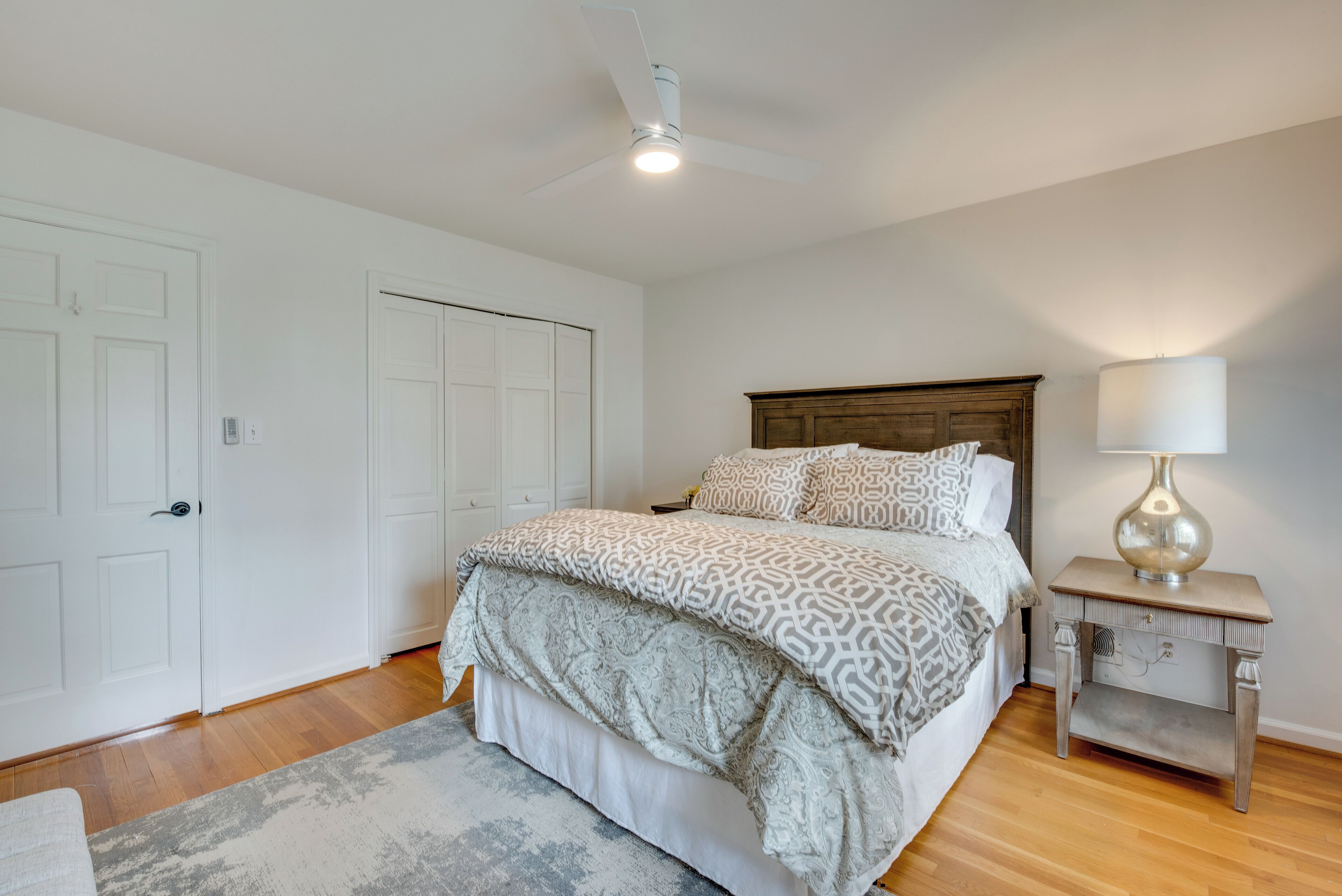 A bedroom with a bed, a nightstand, a lamp, and a ceiling fan.