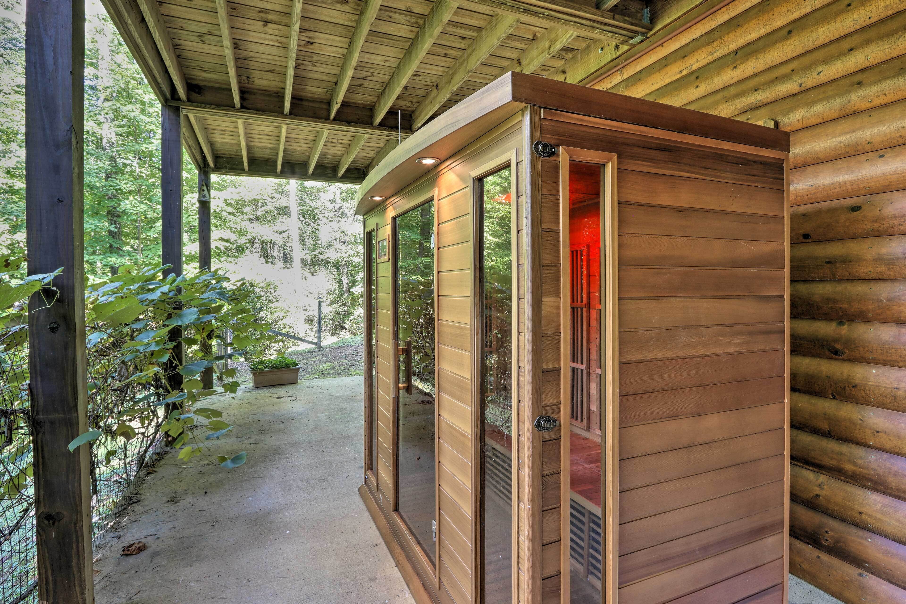 A wooden cabin with a covered porch, large windows, and a door with a red interior.