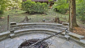 A stone bench with a curved design, surrounded by a stone wall, in a forested area with a wooden building in the background. - Cozy Blue Ridge Cabin w/ Sauna & Trail Access! (Blue Ridge)