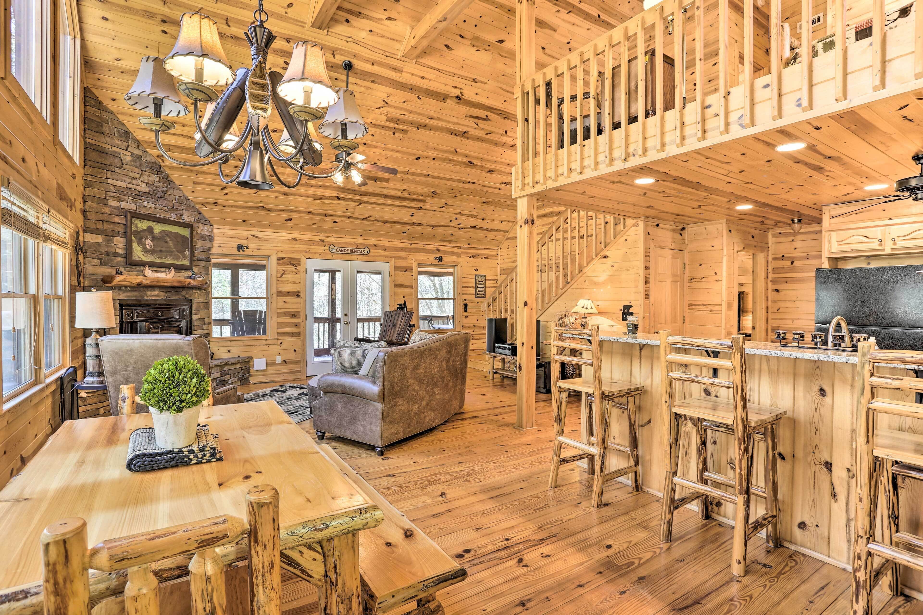 Interior espacioso de una cabaña con comedor, sofá, chimenea y cocina con barra.