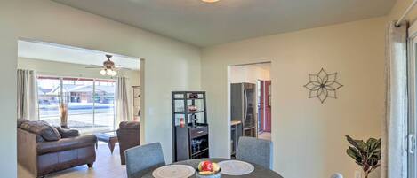 A dining area with a round table, grey chairs, and a fruit bowl.