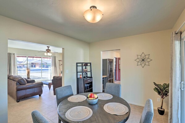 A dining area with a round table, grey chairs, and a fruit bowl.