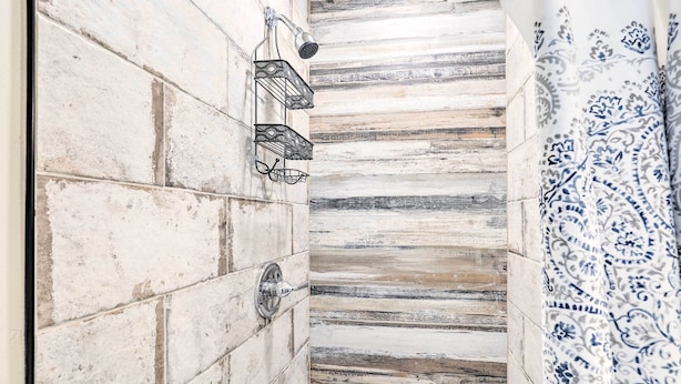 Een badkamer met een betegelde muur, een douche met een handdouche en een decoratief gordijn.