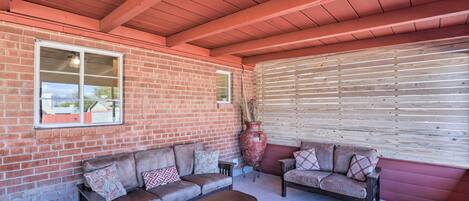 An enclosed patio area with brick walls, wooden ceiling beams, and two sofas with patterned cushions.