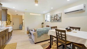 Una cucina moderna con mobili in legno, un'area pranzo con tavolo e sedie e un soggiorno con divano e un quadro.
