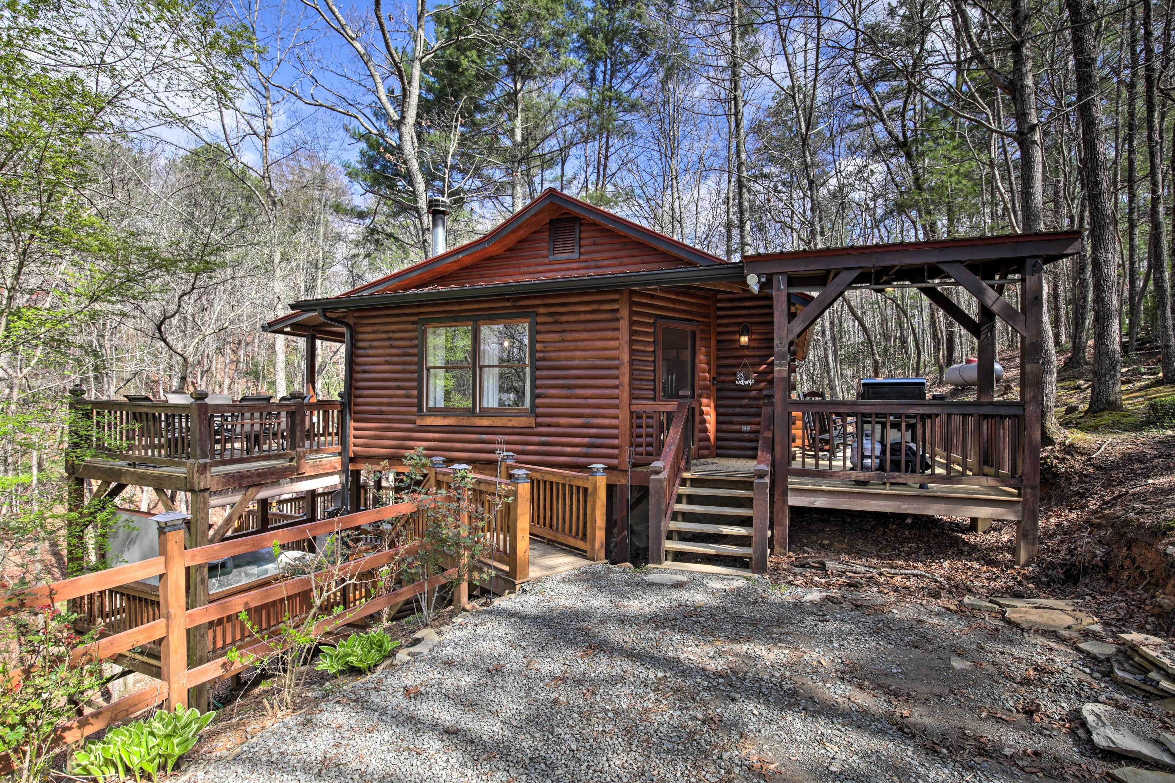 A rustic cabin with a wooden deck, a covered porch, and a gravel driveway.
