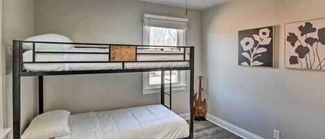 A bunk bed room with a ceiling fan, a window with blinds, a guitar, and two floral wall art pieces.