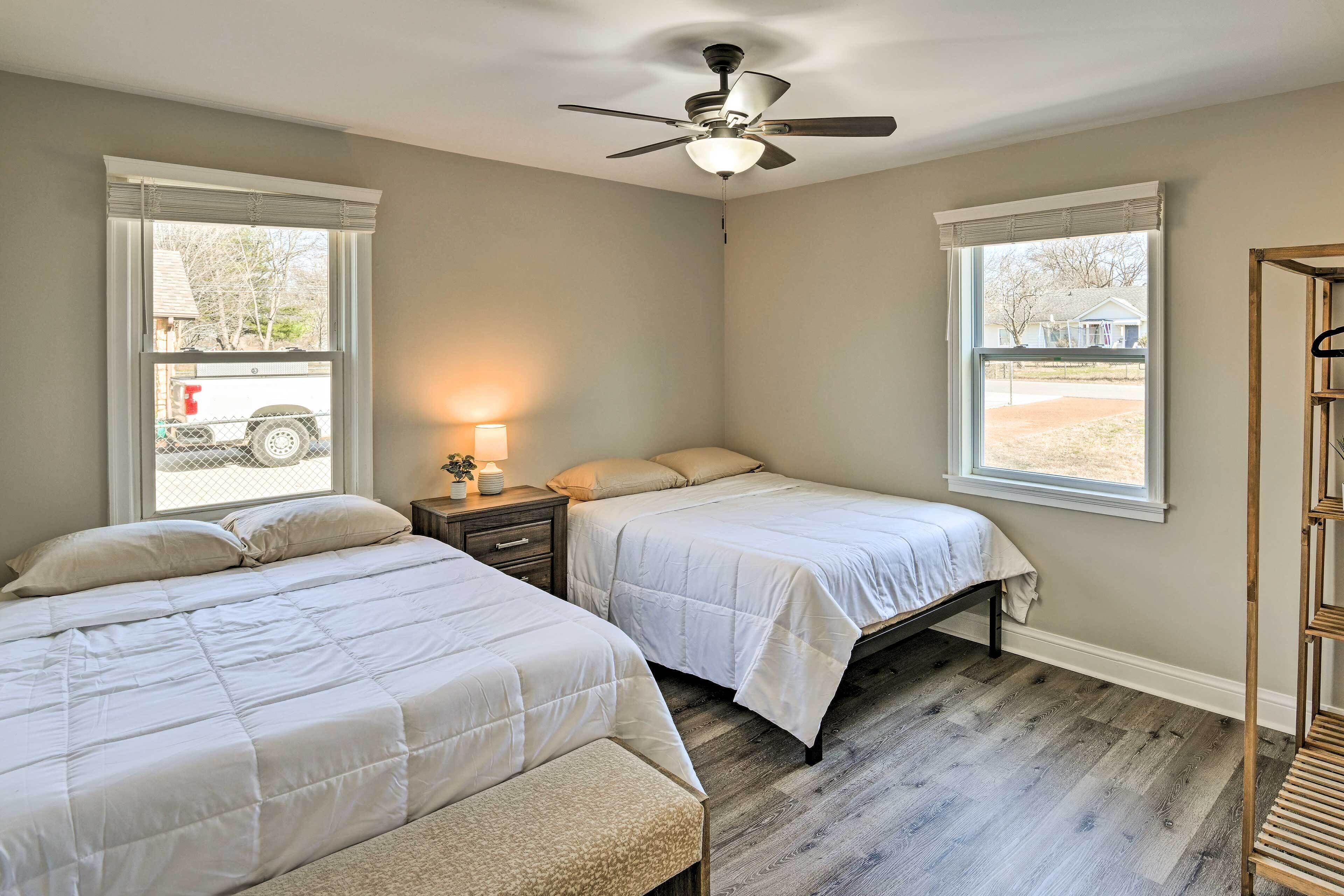 A bedroom with two beds, a ceiling fan, and a window with a view of a parked vehicle outside.