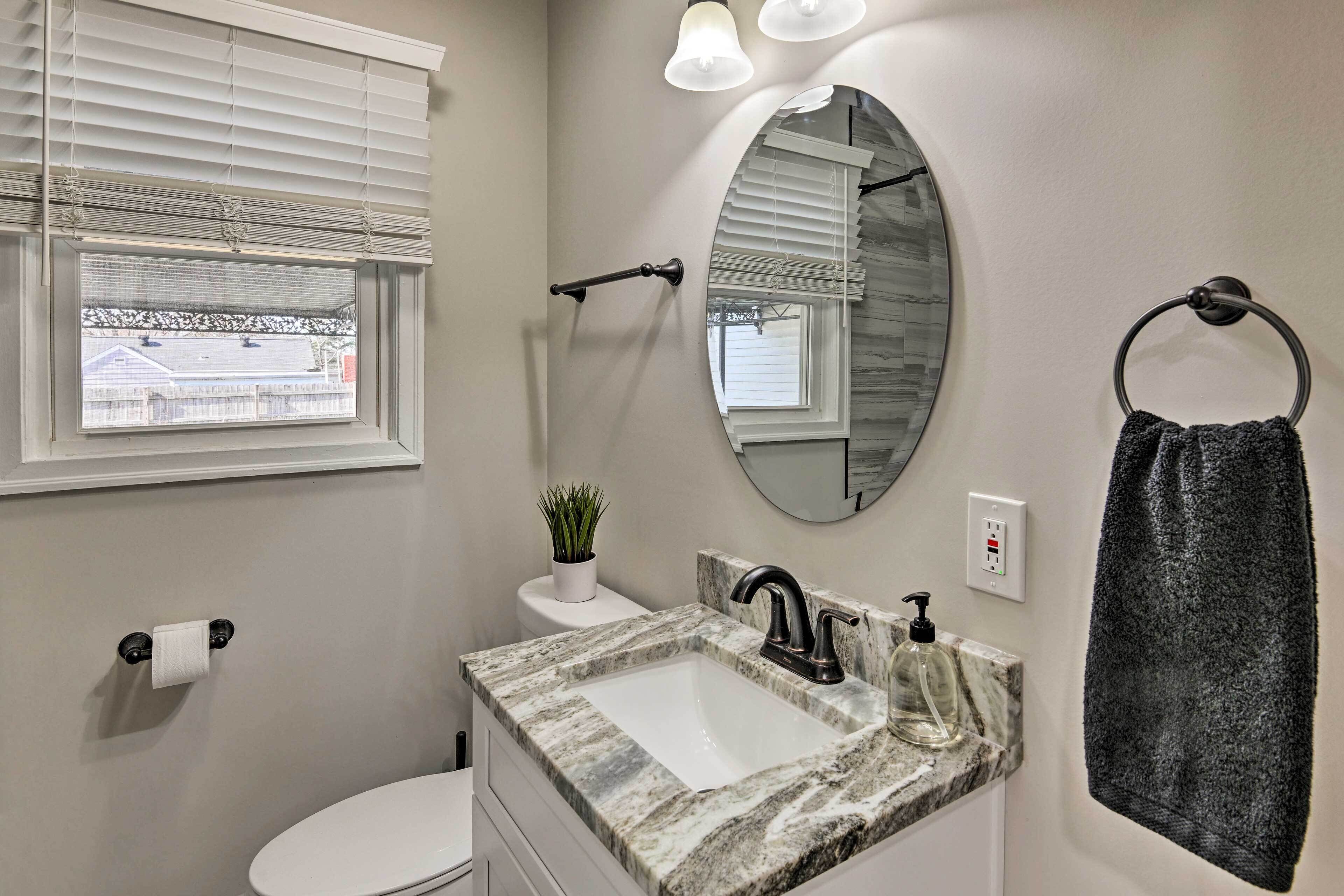 A bathroom with a white toilet, a sink with a marble countertop, a mirror, and a towel rack.