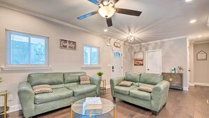 A living room with two green leather sofas, a glass coffee table, and a ceiling fan.
