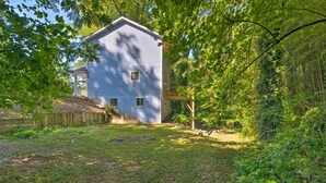 A house with a covered porch, a fenced yard, and dense surrounding vegetation.