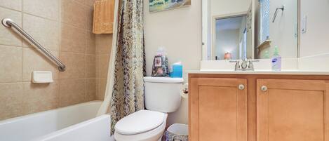Une salle de bain avec une baignoire, des toilettes, un rideau de douche et des meubles en bois.