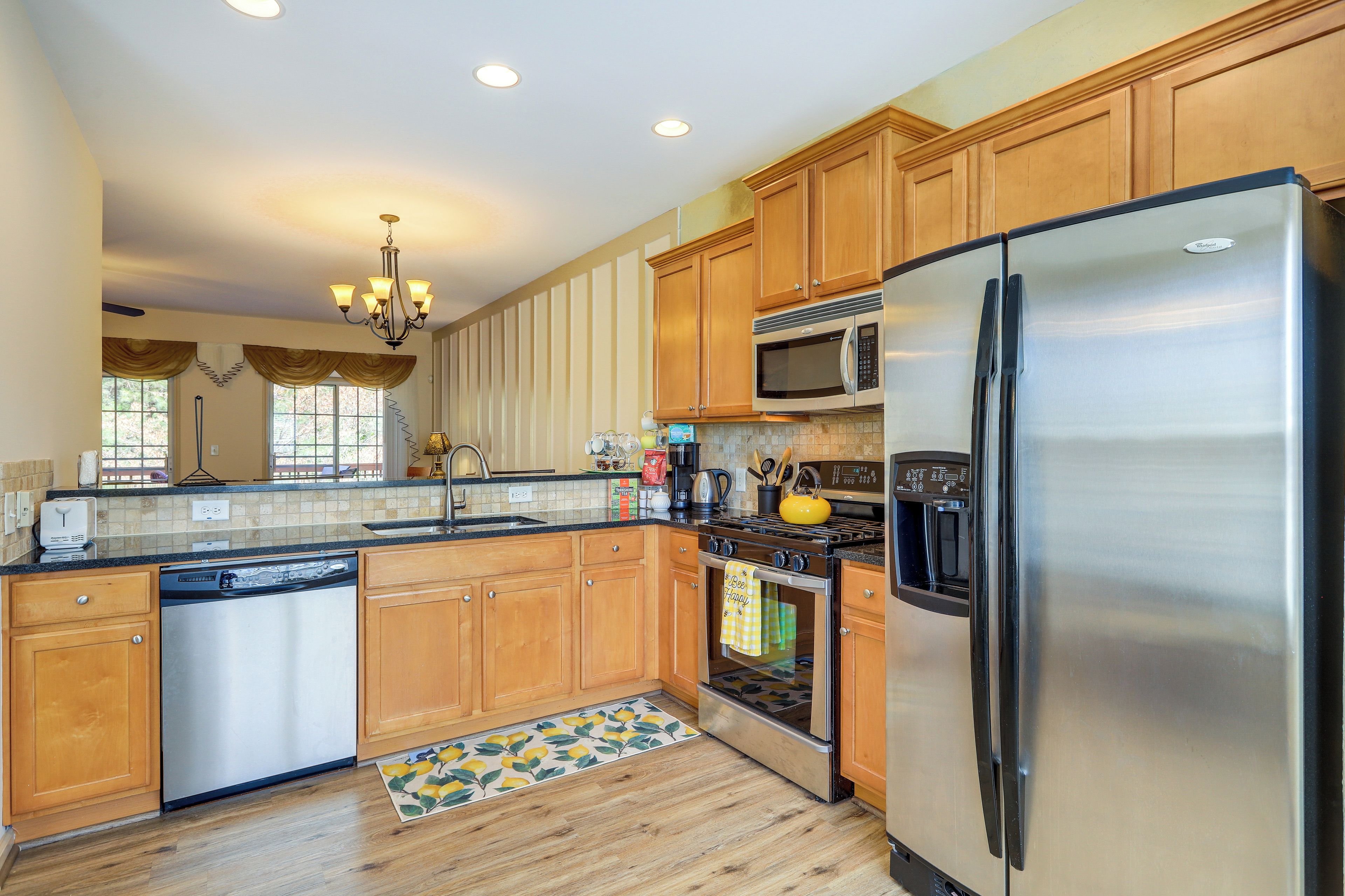 A kitchen with wooden cabinets, stainless steel appliances, a chandelier, and a patterned floor runner.